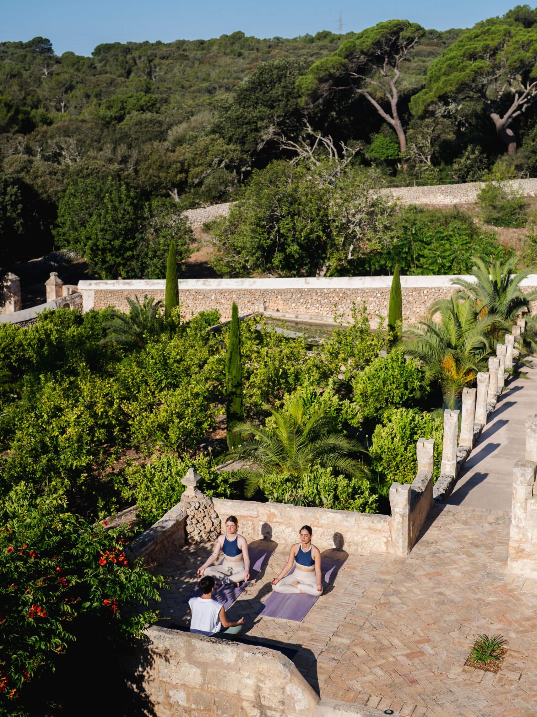 Zwei Frauen praktizieren Meditation auf sonniger Dachterrasse mit Natursteinmauern und mediterraner Vegetation im Chōju Retreat Menorca
