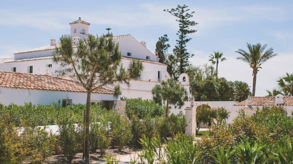Weitläufige weisse Finca des Chōju Retreat mit terrakottafarbenen Ziegeldächern inmitten üppiger mediterraner Gartenanlage auf Menorca