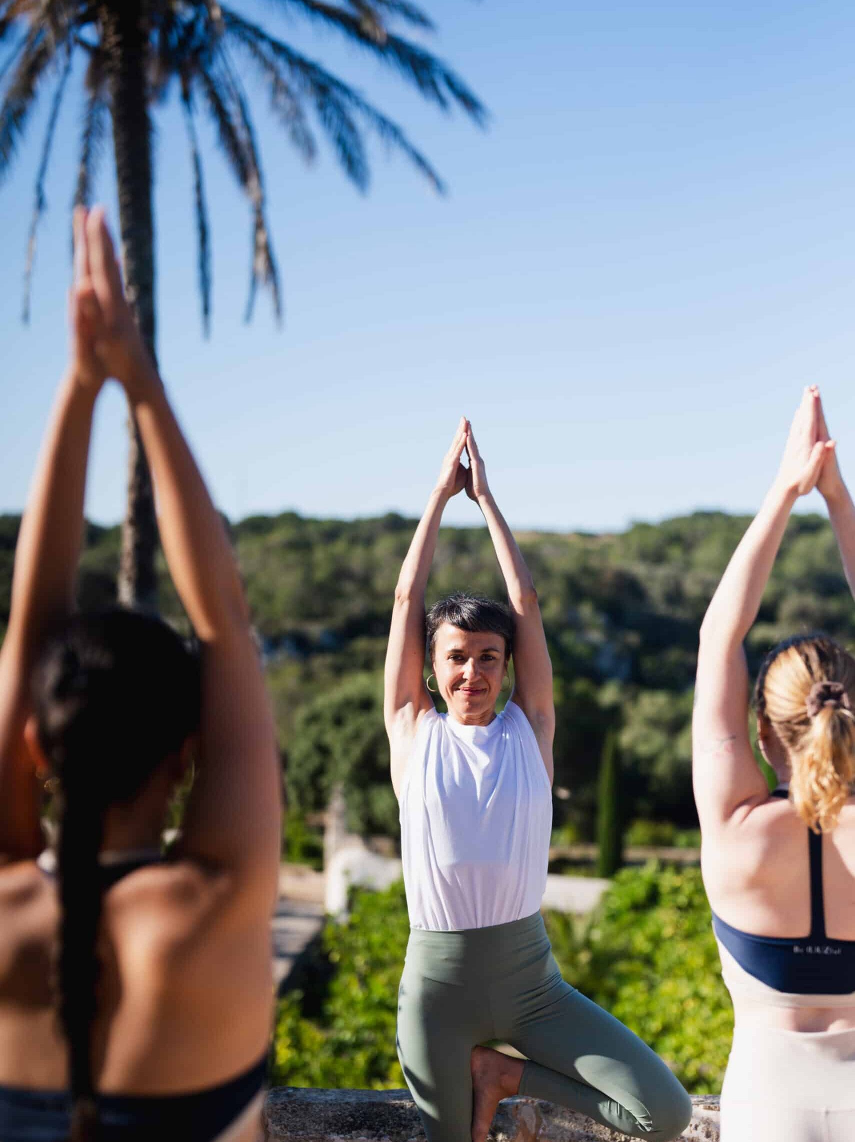 Yoga-Session im Freien mit Instruktorin und Teilnehmern in mediterraner Gartenlandschaft auf Menorca
