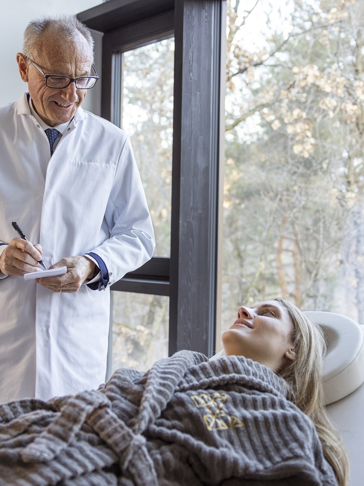 Arzt in wessem Kittel führt medizinische Konsultation mit Patientin in lichtdurchflutetem Behandlungsraum durch