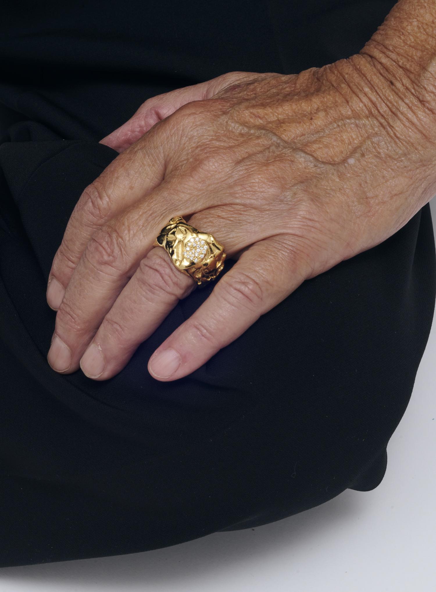 Ein prachtvoller goldener Ring mit Diamanten aus der Fine Edition von Yan Jiang ziert eine Hand, die elegant auf dunklem Stoff ruht.