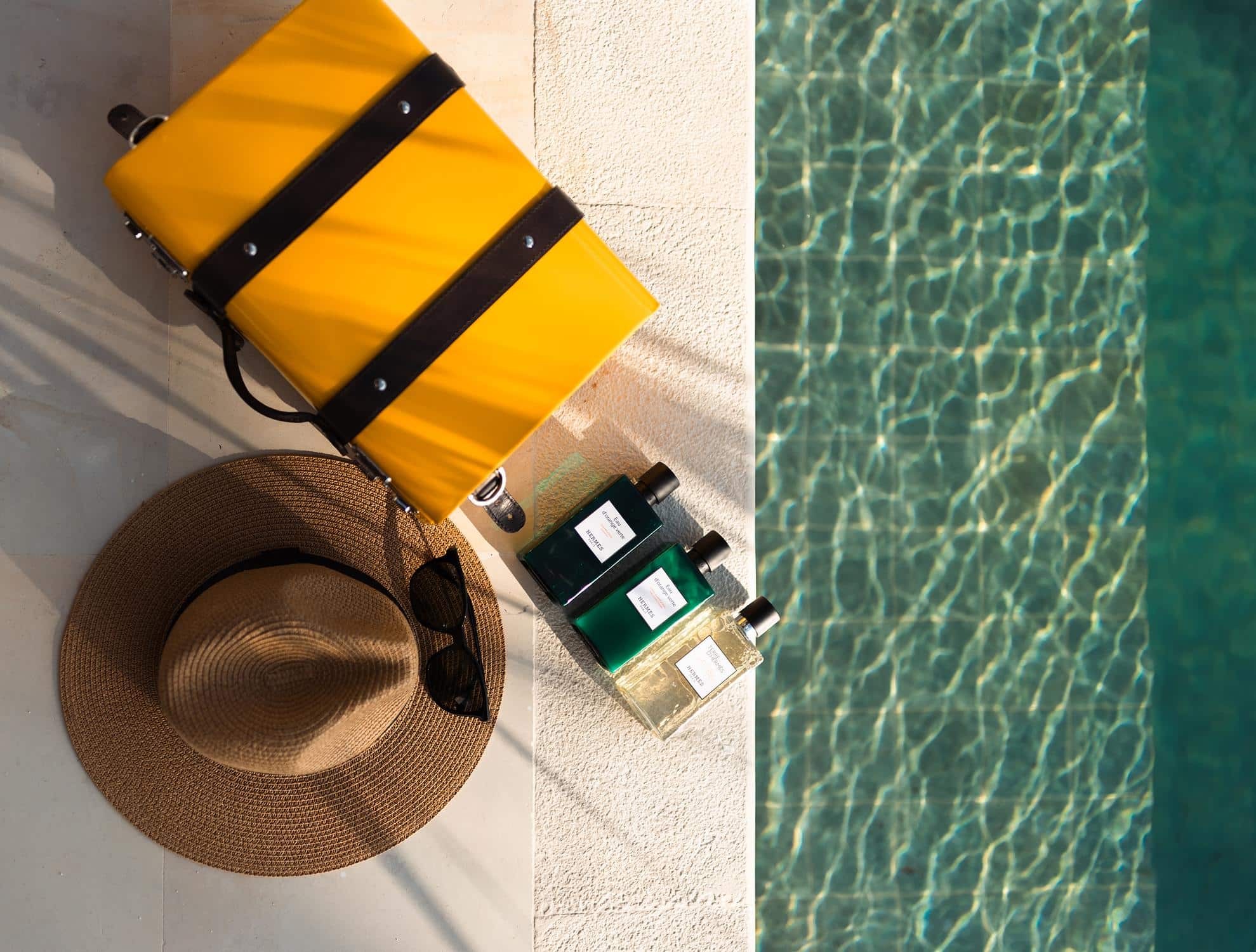 Die Essenz eines luxurioesen Urlaubs auf den Malediven: Ein eleganter Koffer, Sonnenhut und erlesene Duefte liegen bereit am funkelnden Pool.