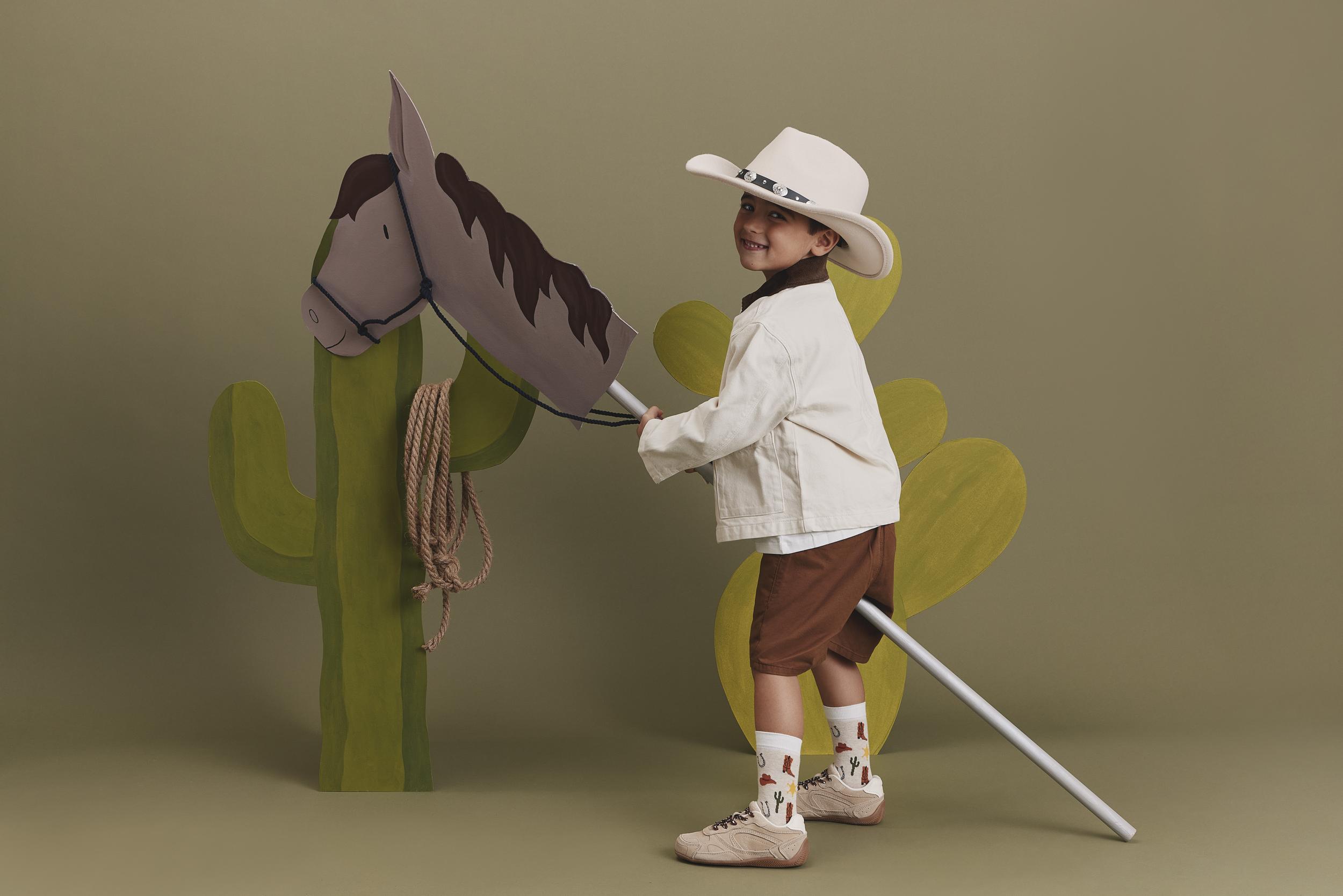 Mit einem breiten Grinsen galoppiert der kleine Cowboy auf seinem Steckenpferd ins Abenteuer, passend gekleidet in FALKE Legwear SS26.