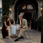 Ein elegantes Paar genieSSt einen lebhaften Austausch auf einer idyllischen Terrasse, wahrend ihre anspruchsvollen Strumpfe und Socken den stilvollen FALKE SS26-Look perfekt erganzen.