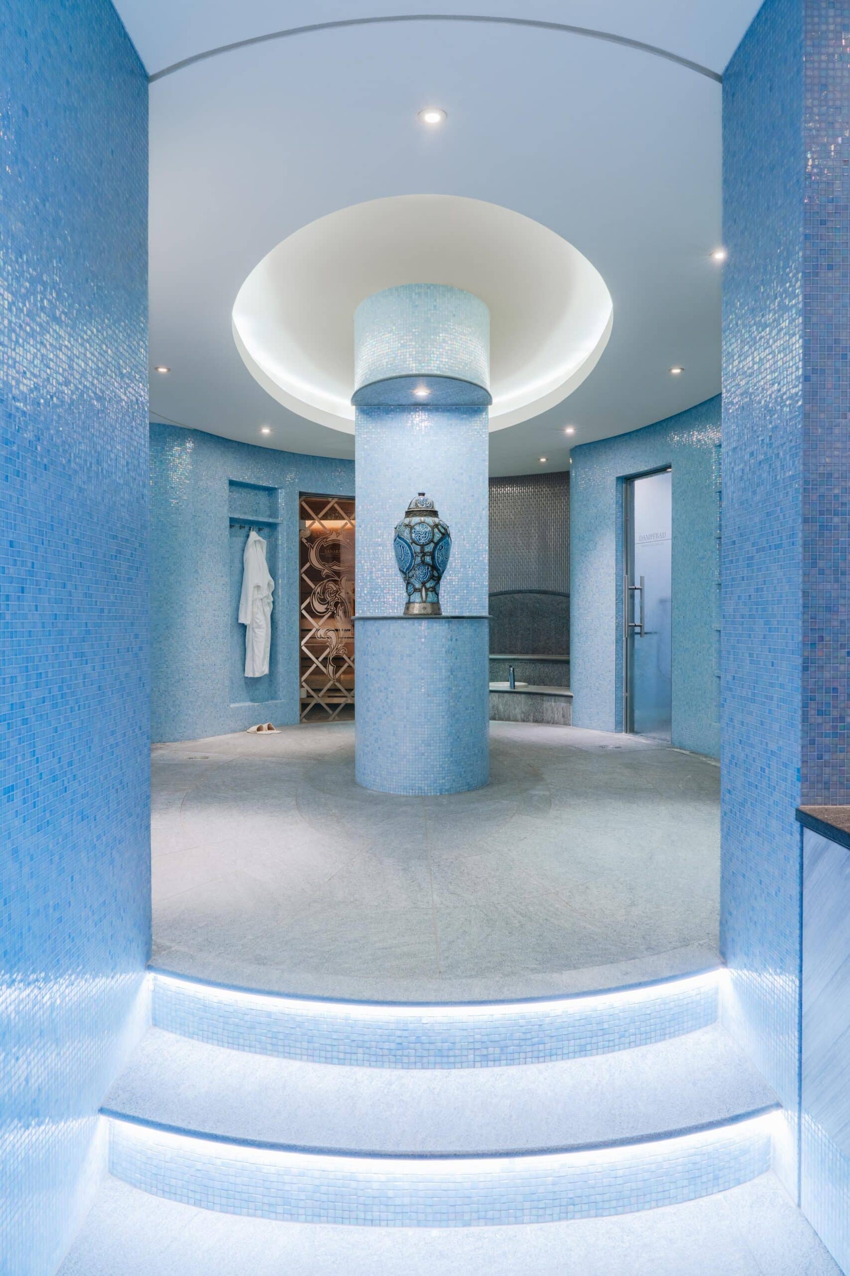 Blaue Mosaikfliesen und sanfte Lichtakzente schaffen in diesem runden Dampfbadbereich eine Oase der Ruhe und modernen Hotellerie.