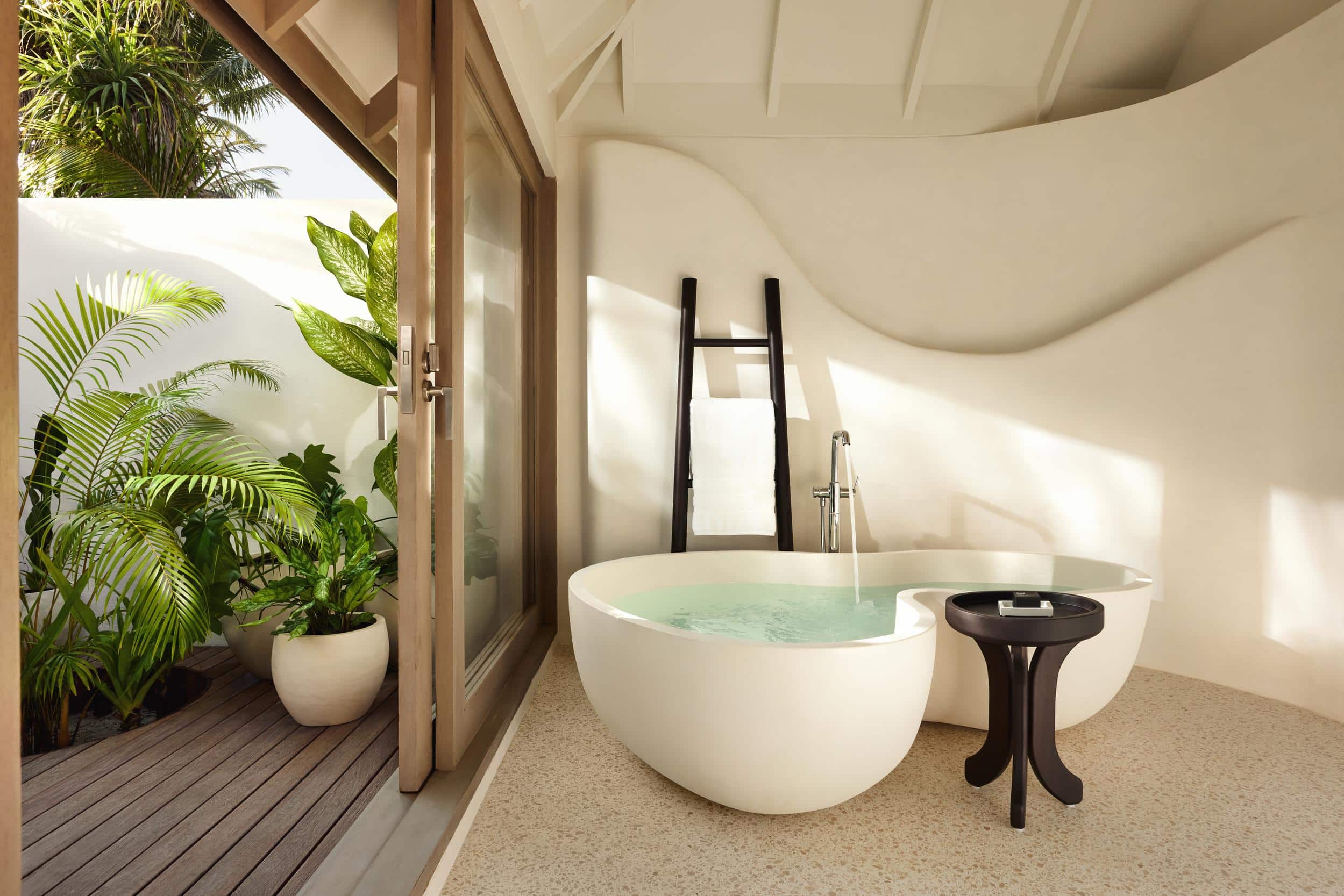 Frisches Wasser fullt die freistehende Badewanne in der Temptation Beach Pool Villa des LUX* South Ari Atoll, wahrend tropisches Grune durch die offene Tur lockt.