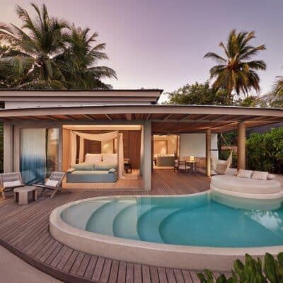Erleben Sie einen ruhigen Abend in der Temptation Beach Pool Villa des LUX* South Ari Atoll, wo sich private Poollandschaft und elegantes Interieur unter dem rosa Abendhimmel vereinen.