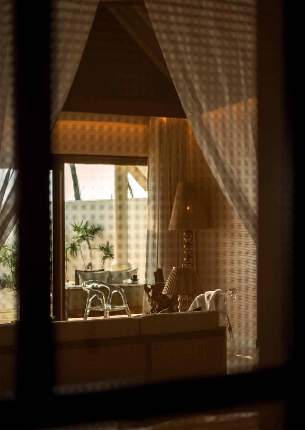 Sanfte Schattenmuster fallen durch die filigranen Vorhänge und beleuchten das stilvolle Innere einer tropischen Villa auf den Malediven.