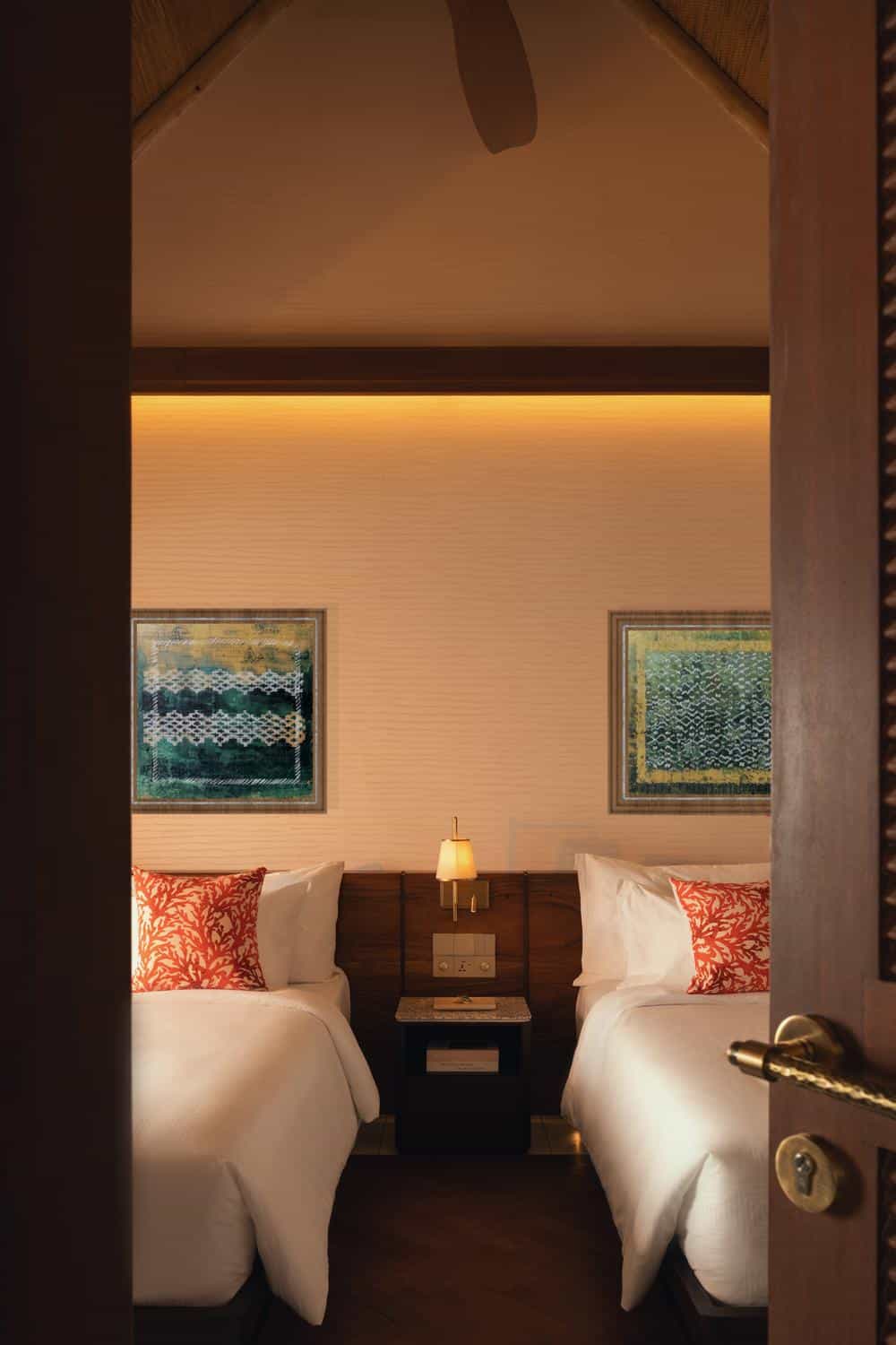 Der Blick durch die leicht geöffnete Tür enthüllt ein stilvolles Schlafzimmer auf den Malediven, das mit warmen Lichtern und beruhigenden Mustern zum Verweilen einlädt.