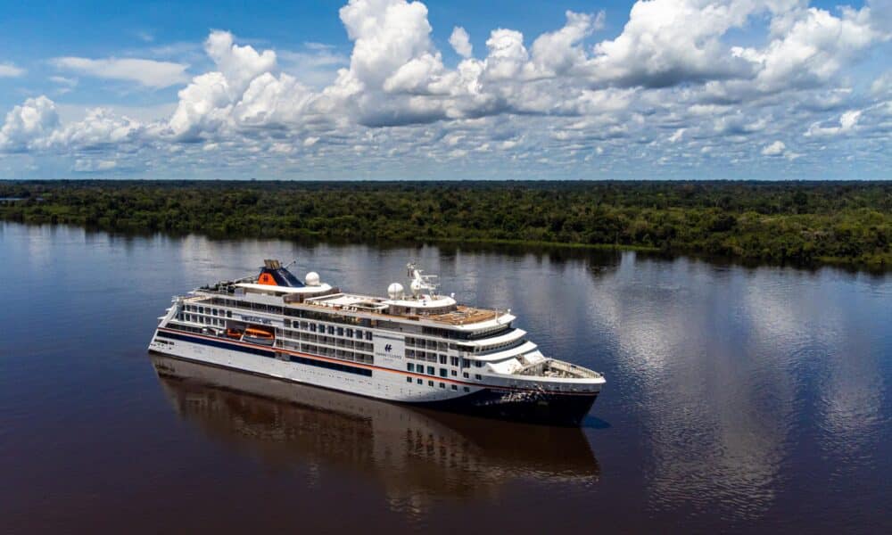 Die HANSEATIC spirit von Hapag-Lloyd Cruises navigiert auf dem dunklen Wasser des Amazonas, umgeben vom dichten, grunen Regenwald unter einem weit gespannten Himmel.
