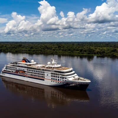 Die HANSEATIC spirit von Hapag-Lloyd Cruises navigiert auf dem dunklen Wasser des Amazonas, umgeben vom dichten, grunen Regenwald unter einem weit gespannten Himmel.